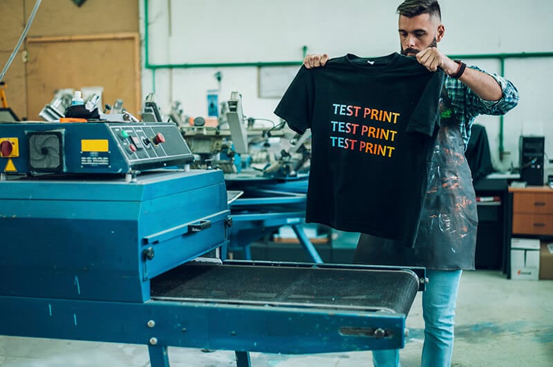 Operatore pone maglietta stampata in serigrafia in un forno a tunnel